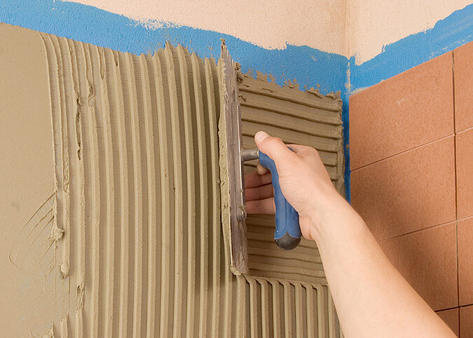Fliesen an die Wand kleben gleichmäßiges Verteilen des Fliesenklebers mit Zahnkelle für optimale Haftung der Wandfliesen
