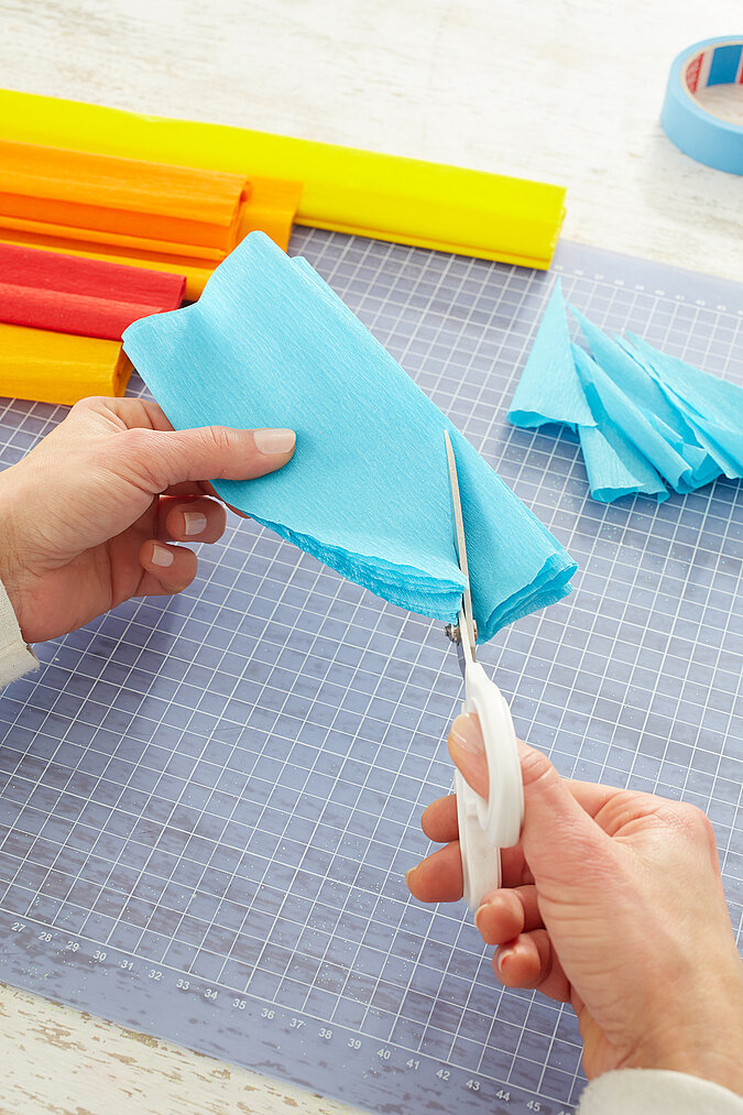 Gefalteter, blauer Krepppapierstreifen wird an einer Seite mit einer Schere abgerundet