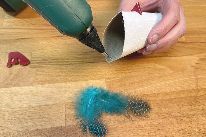 Heissklebepistole bestreicht eine geoeffnete und zum Basteln bemalte Toilettenpapierrolle mit Kleber