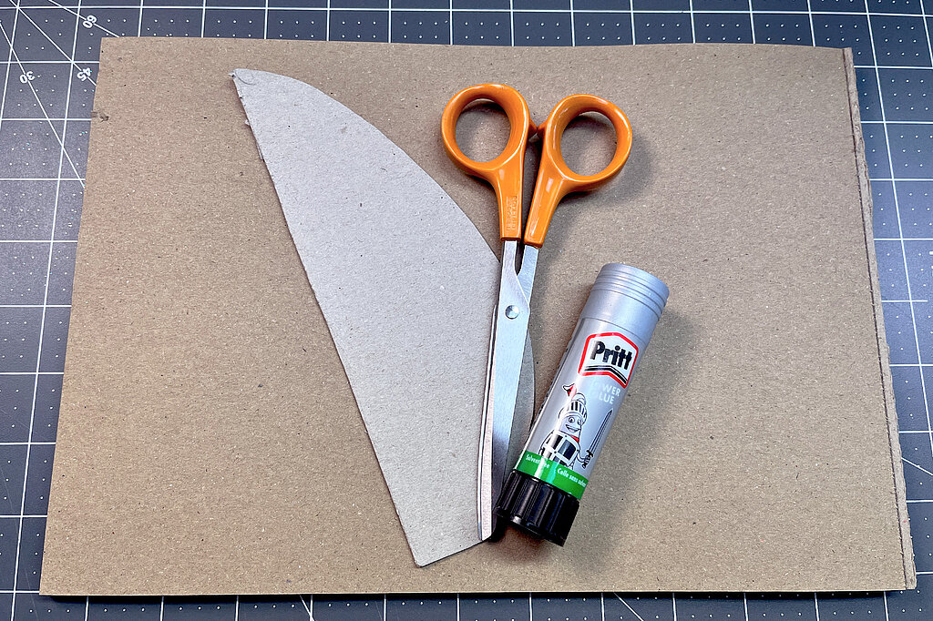 Hände zeichnen mit weißem Stift die Kontur einer Papierschablone auf braunes Kartonpapier nach
