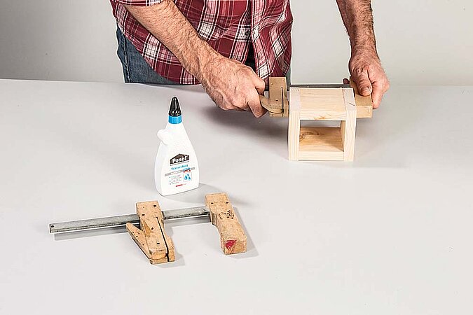 Verleimtes Holzregal für den Raumteiler aus Birkenstämmen wird mit Schraubzwingen fixiert