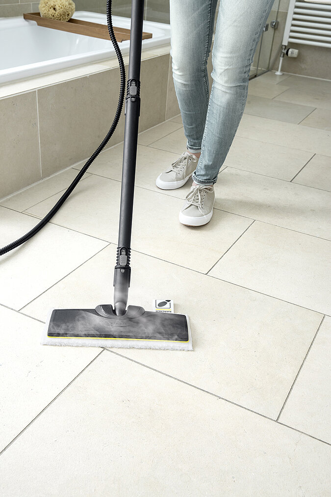 Bildausschnitt mit Dampfreiniger der Fliesenboden abdampft im Hintergrund die Fuesse einer Frau