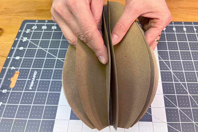 ovale, mittig zusammengklebte Papierformen werden wie ein Faecher aufgeklappt 