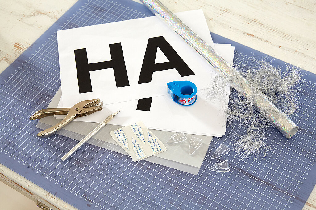 Materialien, um die Silvestergirlande zu basteln: ausgedruckte Buchstaben, Klebehaken, tesafilm, Cutterfilm, Schneidmatte
