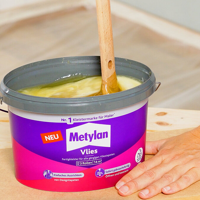 Wände richtig tapezieren: Gebrauchsfertiger Metylan Vlies-Kleister wird mit Holzstab aufgerührt – ideal zum schnellen Start mit Vliestapeten ohne Anrühren