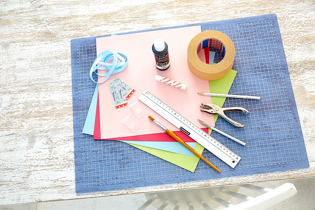 Einschulung Wimpelkette DIY-Materialien mit Papier, Klebeband, Lineal und Bastelwerkzeug auf Schneidematte vorbereitet