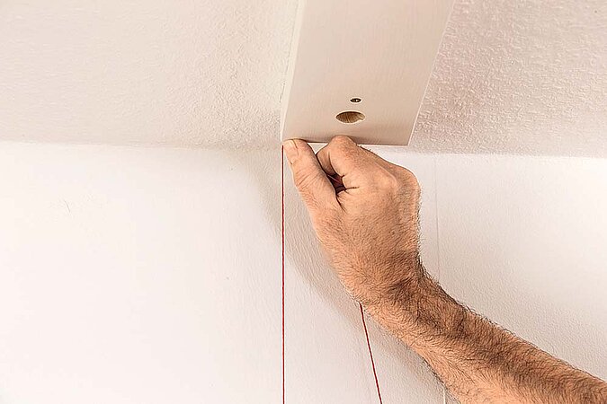 Mit einer Lotschnur wird die Position des unteren Holzbretts für einen Raumteiler aus Birkenstämmen von der Decke auf den Boden übertragen