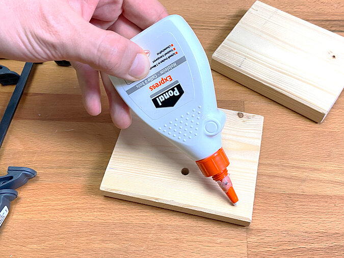 Holzleim wird auf eine gebohrte Holzplatte aufgetragen – Vorbereitung zur Verbindung der Podestteile für die DIY LED-Leute aus Getränkedose.