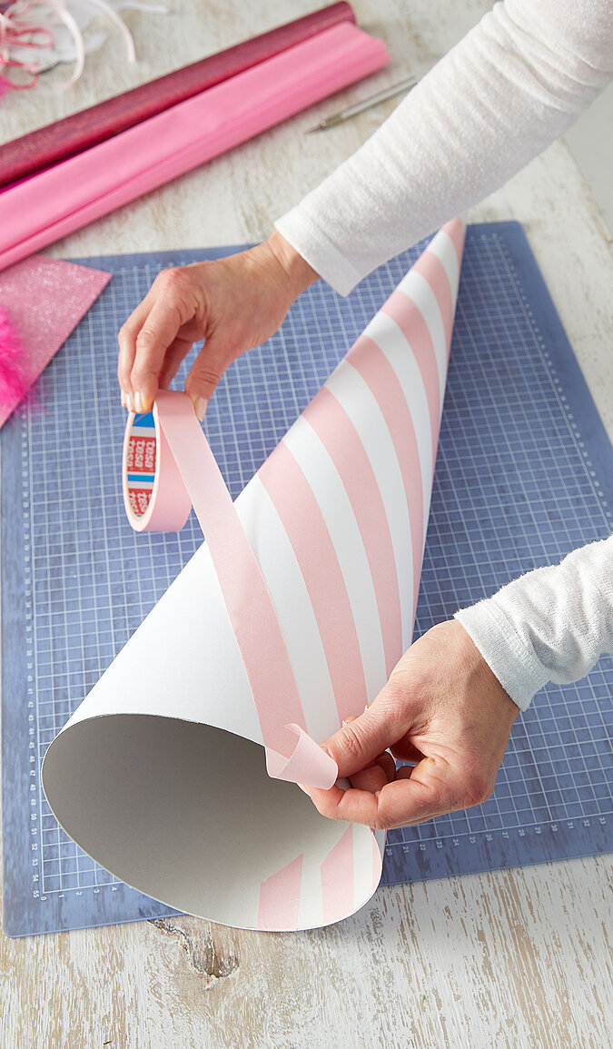 Auf einen weißen Schultüten-Rohling werden rosa Malerkrepp-Streifen für den Einhorn-Look geklebt