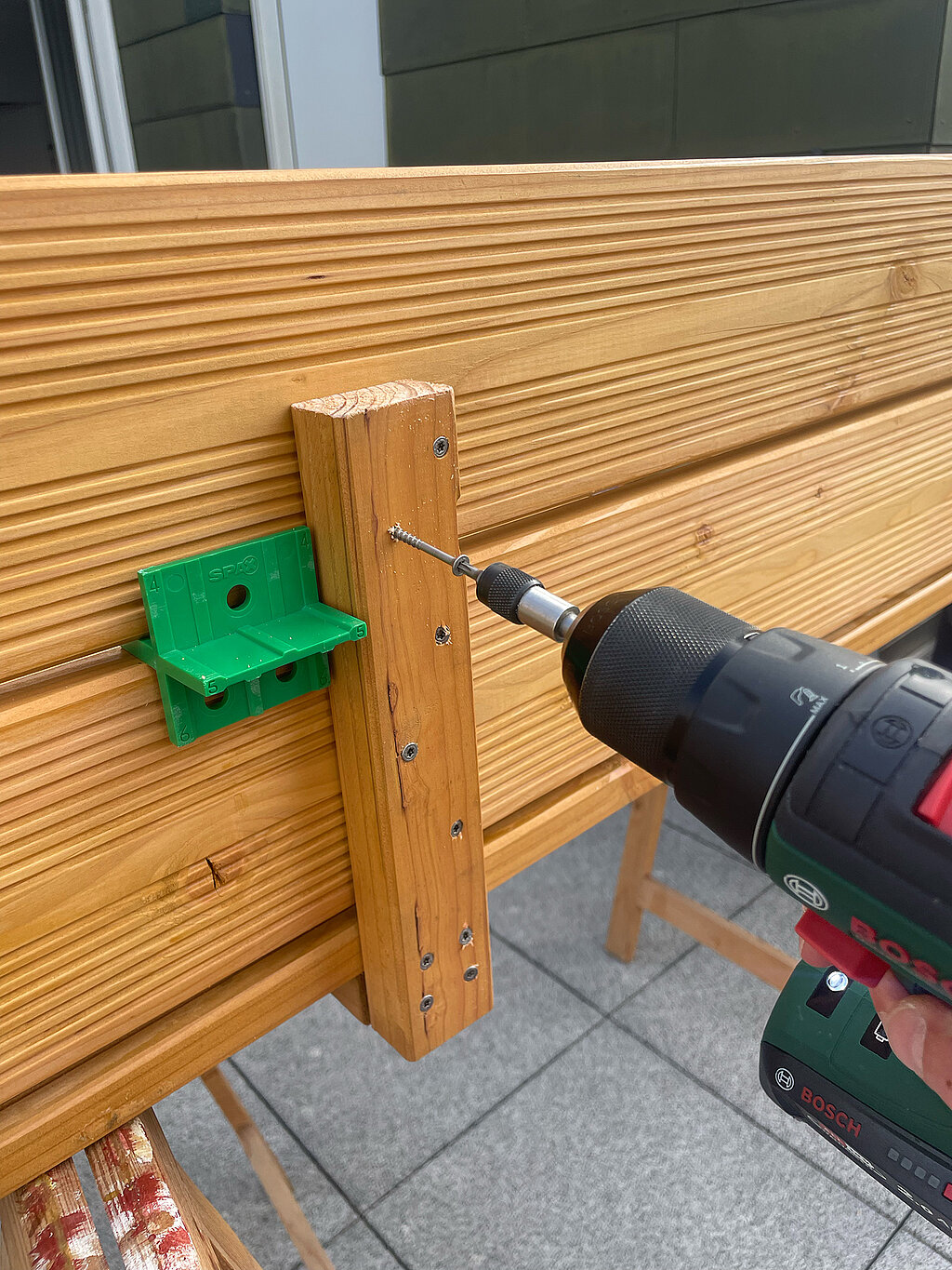 Grillplatz für die Terrasse bauen: Befestigung eines senkrechten Holzstücks an der Rückwand der Ablage mit Akkuschrauber – sorgt für zusätzliche Stabilität bei der Montage der DIY-Grillstation.