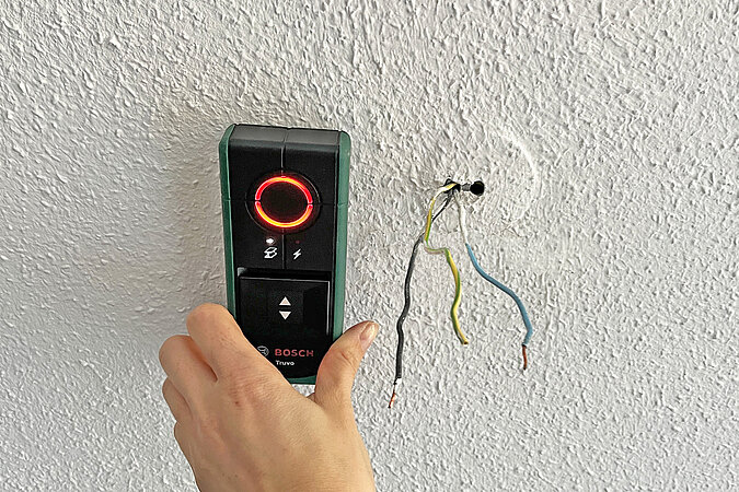 Die Decke wird mit dem Leitungs- und Stromprüfer Truvo von Bosche überprüft, um die Halterung für die Lampe in einer sicheren Zone anzubringen. Die Lampe zeigt rot an.