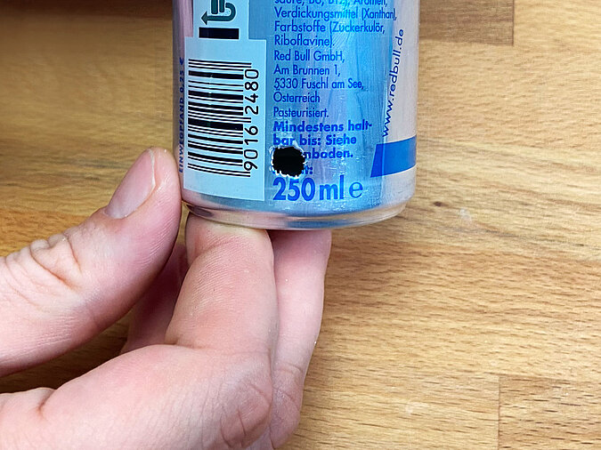 Nahaufnahme der Öffnung am unteren Rand einer Red-Bull-Dose für die Einführung der Lichterkette – vorbereitet zum Einführen der Lichterkette.