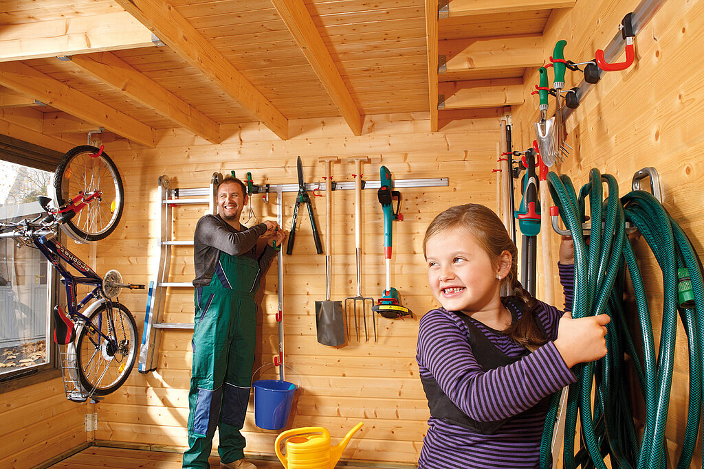 Gärtnern ohne Torf im Gartenhaus, Kinder räumen Gartenschläuche und Werkzeuge auf, nachhaltige Gartenorganisation als Teil umweltbewusster Gartenarbeit