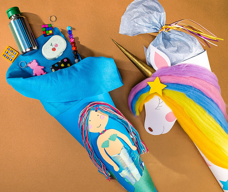 Schultüte basteln mit fertiger Einhorn-Schultüte und bunter Mähne neben Meerjungfrau-Schultüte