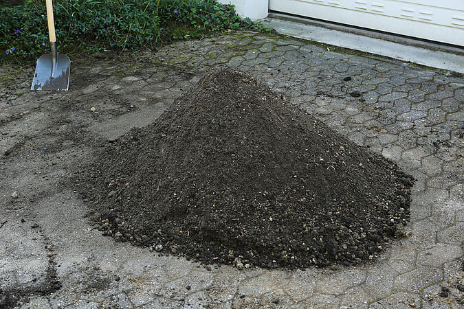 Gärtnern ohne Torf mit einem Haufen torffreier Gartenerde auf gepflastertem Untergrund, nachhaltige Vorbereitung von Erde für umweltfreundliche Gartenarbeit