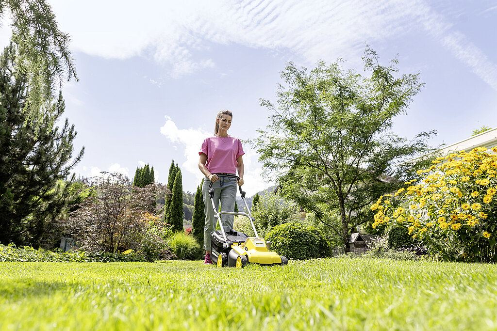Gartenarbeiten Frühling: Rasen im Garten mit einem Rasenmäher mähen und gepflegte Grünfläche im Frühling erhalten