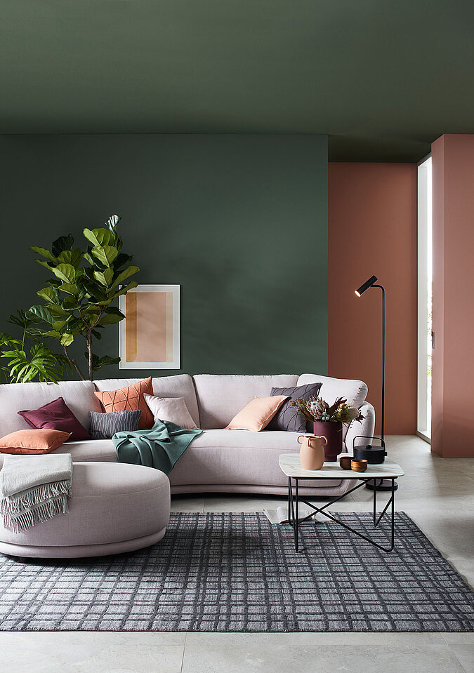 Wunderschönes Wohnzimmerbidl mit rundem Relaxsofa, dekoriert mit Kissen und Decken, sowie Couchtisch und Teppich