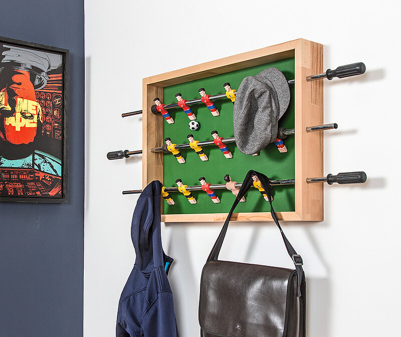 Wandgarderobe aus Kickerfiguren bauen als kreative Garderobe mit Fußballfiguren und Holzrahmen an der Wand befestigt