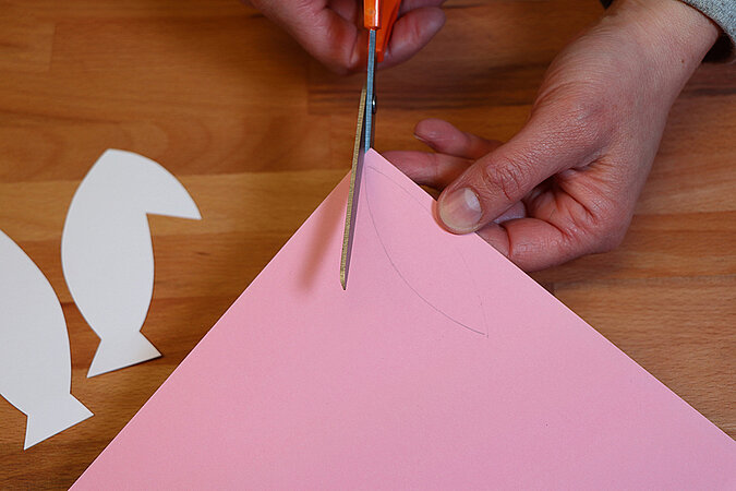 Rosa Tonpapier wird entlang der aufgezeichneten Linie mit einer orangefarbenen Schere ausgeschnitten