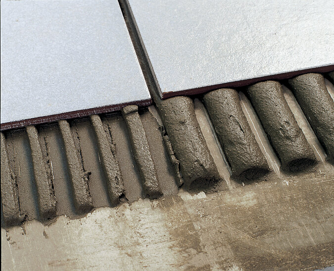 Zwei weiße Bodenfliesen liegen exakt auf einer Schicht Fliesenkleber