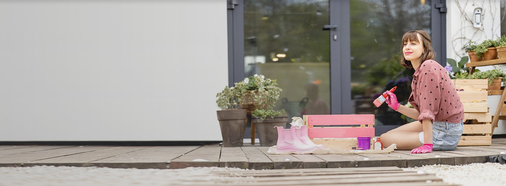 Eine Frau sitzt auf der Terrasse und streicht eine Obstkiste pink an