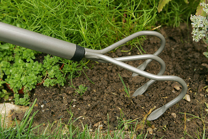 Gartenarbeiten Frühling: Handkralle lockert Erde im Beet zur Vorbereitung der Bepflanzung im Frühling