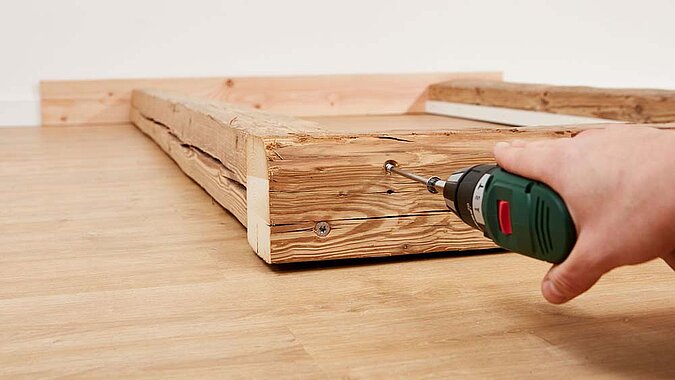 Dicke Holzbalken werden mit einer weiß lackiertes Leiste verschraubt