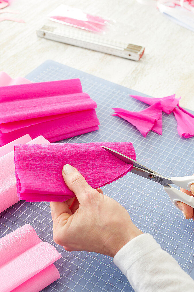 Gefalteter, pinker Krepppapierstreifen wird an einer Seite mit einer Schere abgerundet