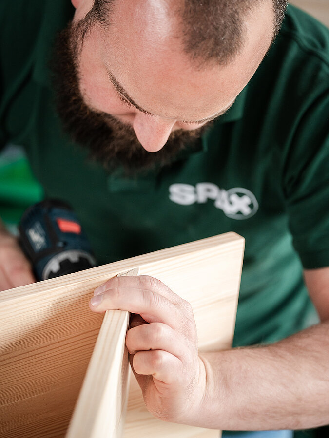 Für eine Helmgarderobe verschraubt ein Mann 3 Bretter zu einem Dreieck zusammen