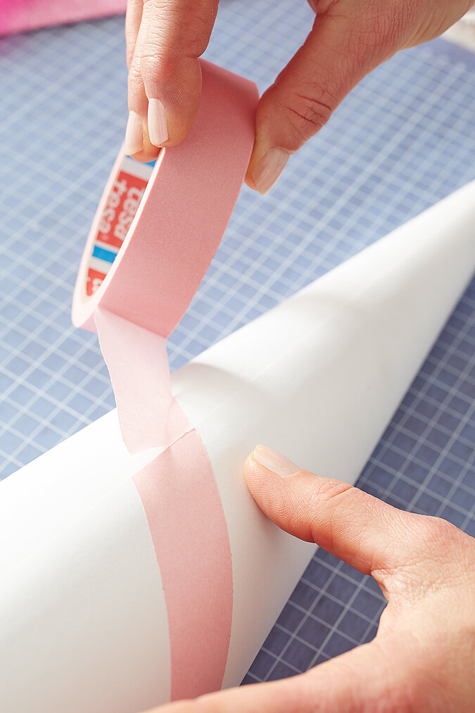 Auf einen weißen Schultüten-Rohling werden rosa Malerkrepp-Streifen für den Einhorn-Look geklebt