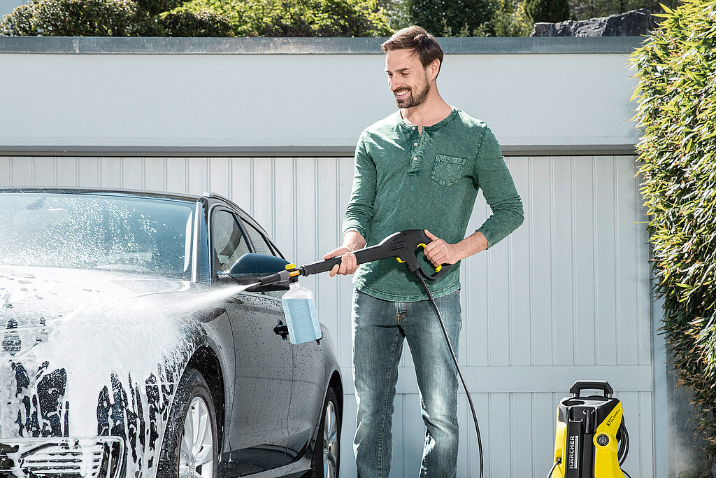 Auto selbst waschen vor der Garage mit Hochdruckreiniger – Mann reinigt silbernen Audi mit Schaum, Tipps für gründliche Autowäsche und Fahrzeugpflege im eigenen Zuhause.
