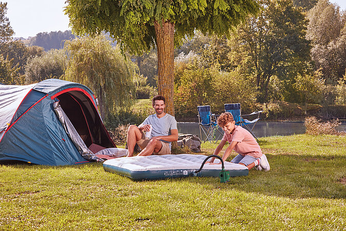 Festival Gadgets elektrische Luftpumpe im Einsatz beim Aufblasen einer Luftmatratze neben Zelt auf dem Campingplatz