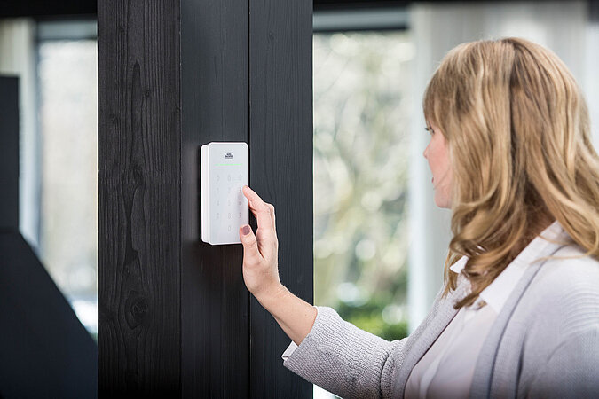 Mythen über richtigen Einbruchschutz – Frau bedient modernes Smart-Home-Alarmsystem mit Touch-Bedienfeld zur Sicherung des Hauses
