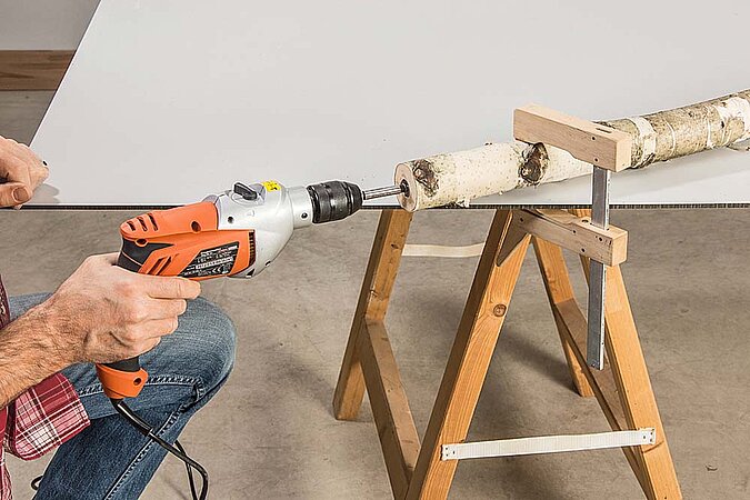 Birkenstamm für einen Raumteiler aus Birkenstämmen wird auf einer Arbeitsfläche mit einem Forstnerbohrer vorgebohrt