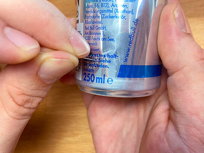 Mit einer Nadel wird ein Loch am unteren Rand einer Red-Bull-Dose gestochen – Vorbereitung für die Lichterkettenöffnung.“
