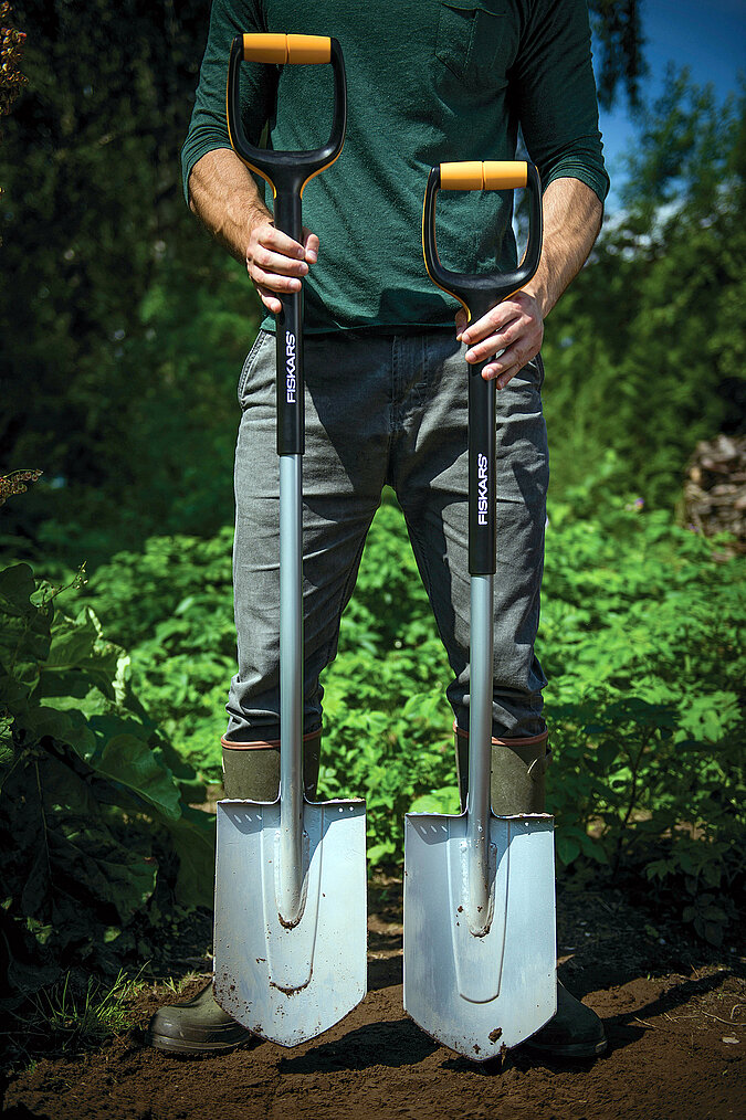 Mann hat zwei unterschiedlich grosse Gartenschaufeln vor sich aufgestellt