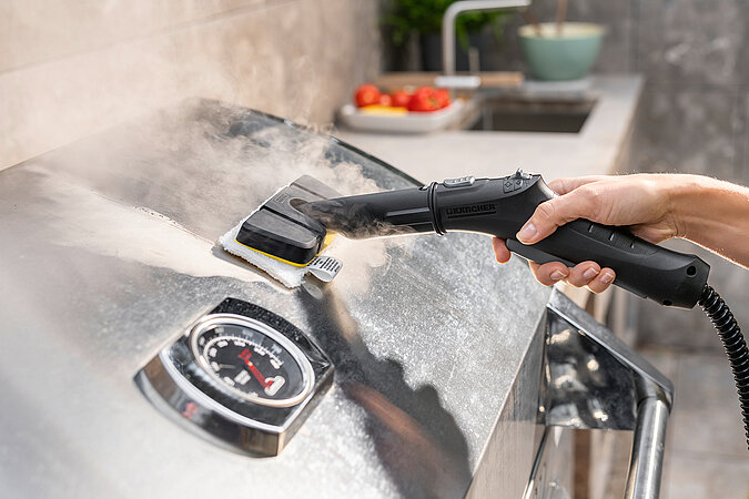 Nahaufnahme einer Reinigung von einer Edelstahlgrillhaube mit einem Dampfreiniger