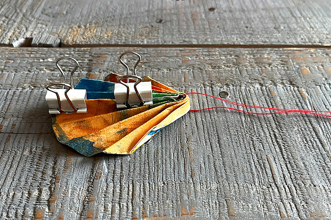 gefaltetes Papier wird mittig zusammengeklebt und mit Klammern fixiert