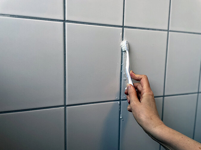 Detailaufnahme einer Hand die mit Zahnbuerste und Hausmittel die Fliesenfugen reinigtugen 