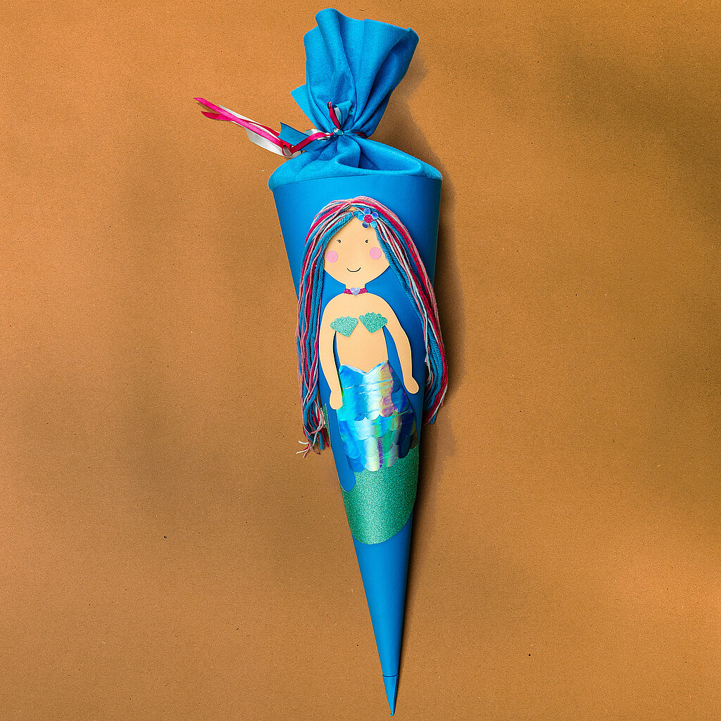 Schultüte Meerjungfrau basteln mit fertiger Meerjungfrauen-Schultüte aus blauem Karton und schimmernder Flosse aus Bastelpapier