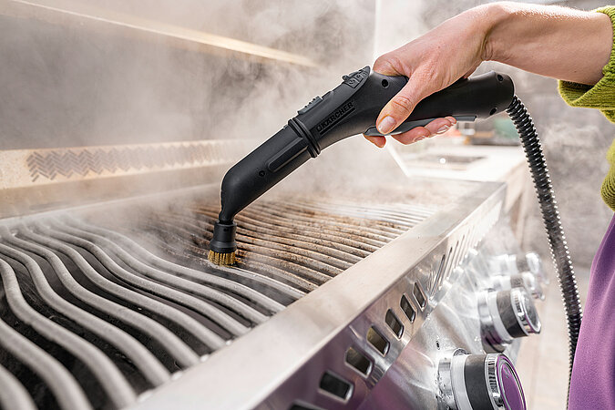 Nahaufnahme einer Reinigung von eines verkrusteten Grillrost mit einem Dampfreiniger