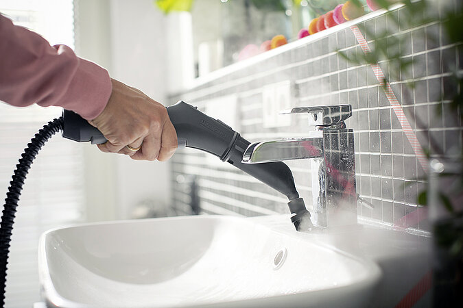 Waschbecken und Armatur im Bad werden von Dampfreiniger mit kleinem Buerstenaufsatz gereinigt