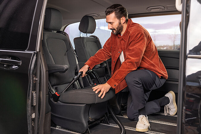 Auto selbst waschen und Innenraum reinigen – Mann saugt die Autositze gründlich aus, um Staub, Krümel und Schmutz aus dem Innenraum zu entfernen.