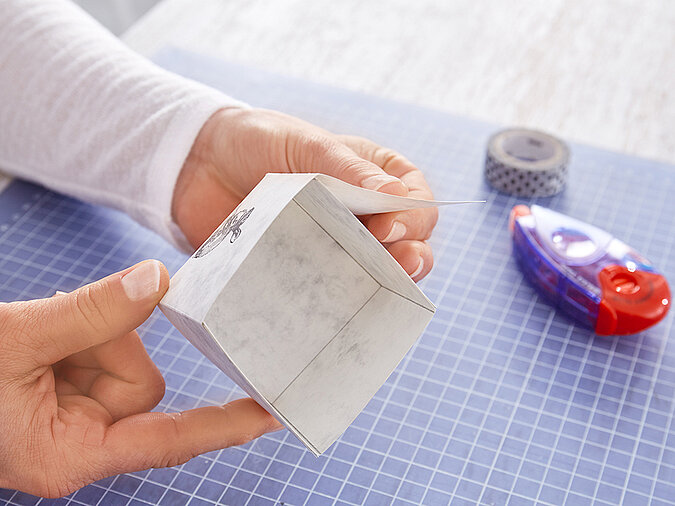 Nahaufnahme einer offenen Papier-Schachtel aus marmoriertem Papier, im Hintergrund liegen Washi-Tape und tesa Kleberoller
