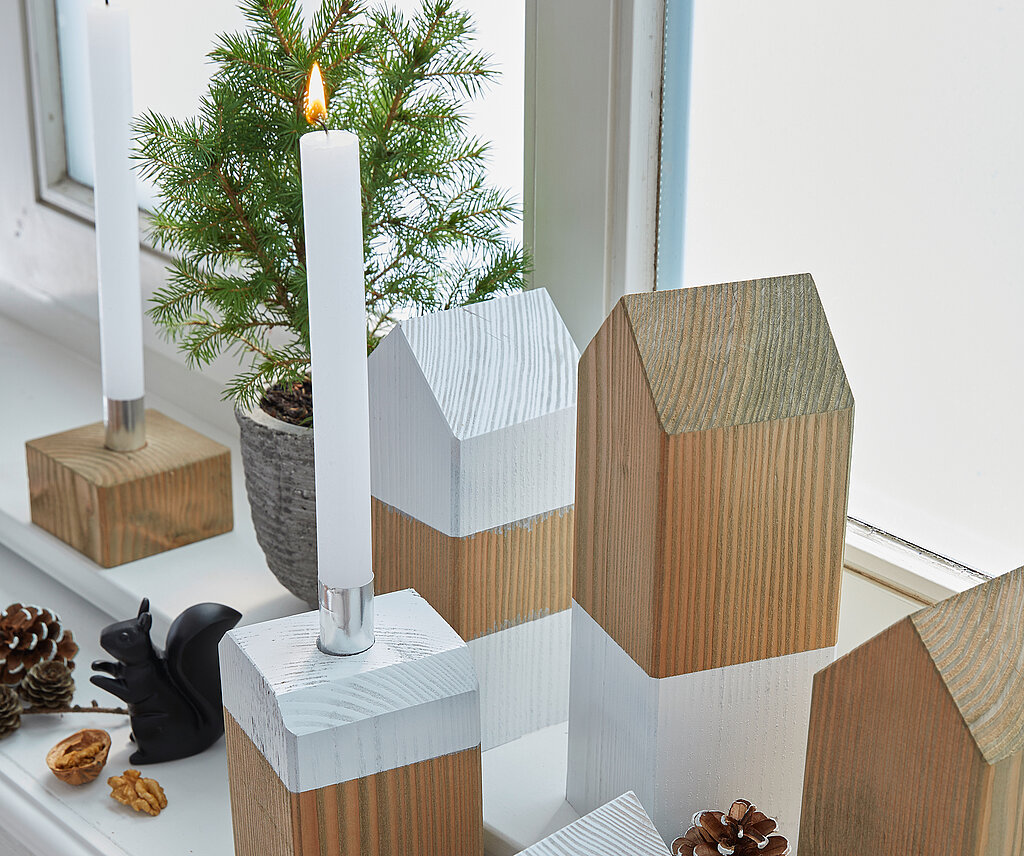 Deko-Häuschen aus Holz stehen festlich dekoriert auf der Fensterbank