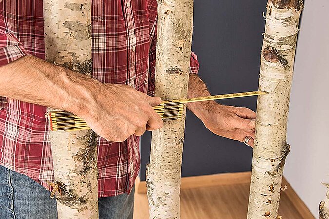 Abstand zwischen den Birkenstämmen des Raumteilers wird mit einem Zollstock ausgemessen