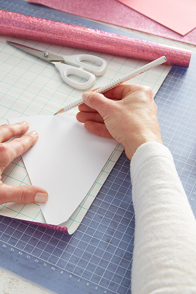 Eine Schultütenspitze wird mit rosafarbener, glitzernder Halogrammfolie beklebt