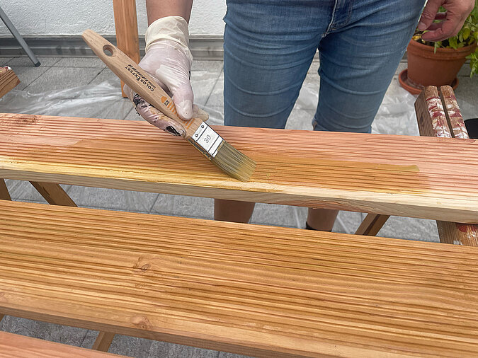 Grillplatz für die Terrasse bauen: Holzlatten werden mit Pinsel und Holzöl versiegelt – wetterfester Schutz für langlebige Bauteile der selbstgebauten Grillstation im Außenbereich.