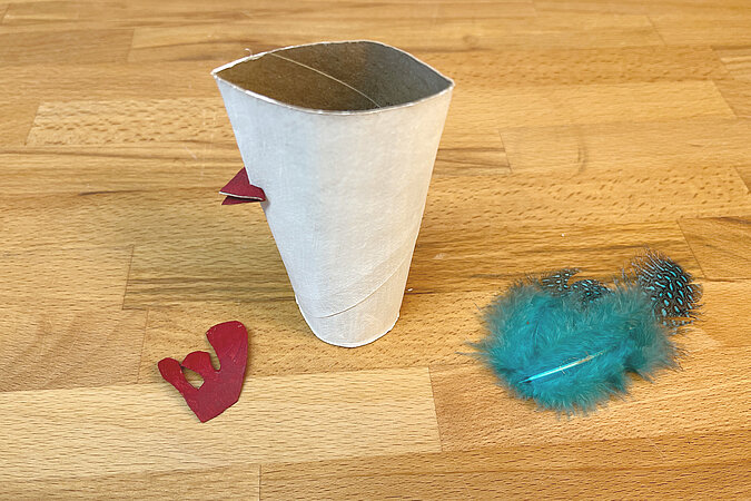 bunte Feder, Hahnenkamm und bemalte Toilettenpapierrolle auf einem Holztisch