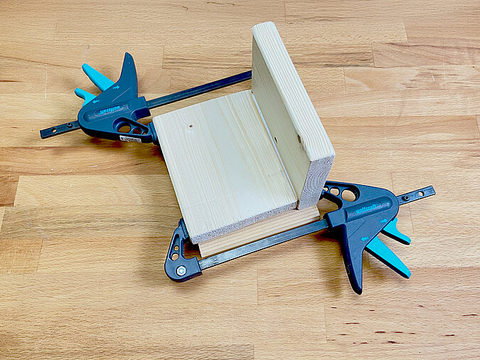 Verleimtes Holzpodest für die DIY LED-Leute aus Getränkedose wird mit zwei Schraubzwingen fixiert und zum Trocknen gepresst.